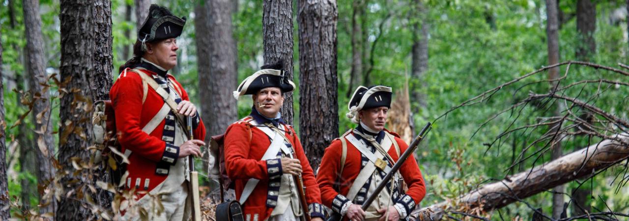 Three British soldiers dressed in uniforms from the American Revolution in a forest.